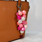 A beaded keychain with a cluster of pink, white, and red beads. The keychain features a variety of bead sizes and textures, including pearls, rhinestones, and heart-shaped beads. A red heart-shaped charm hangs at the bottom.