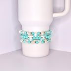A stack of five bracelets made of turquoise blue and white beads. The bracelets are stacked on top of each other and are on a white surface.