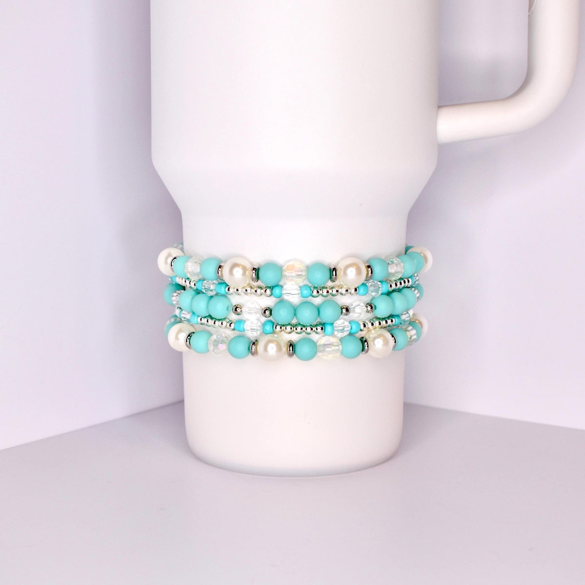 A stack of five bracelets made of turquoise blue and white beads. The bracelets are stacked on top of each other and are on a white surface.