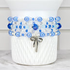 A multi-strand bracelet with blue, white, and clear beads. The bracelet has a silver bow charm hanging from it. The beads are various sizes and shades of blue, with some clear crystal beads interspersed.