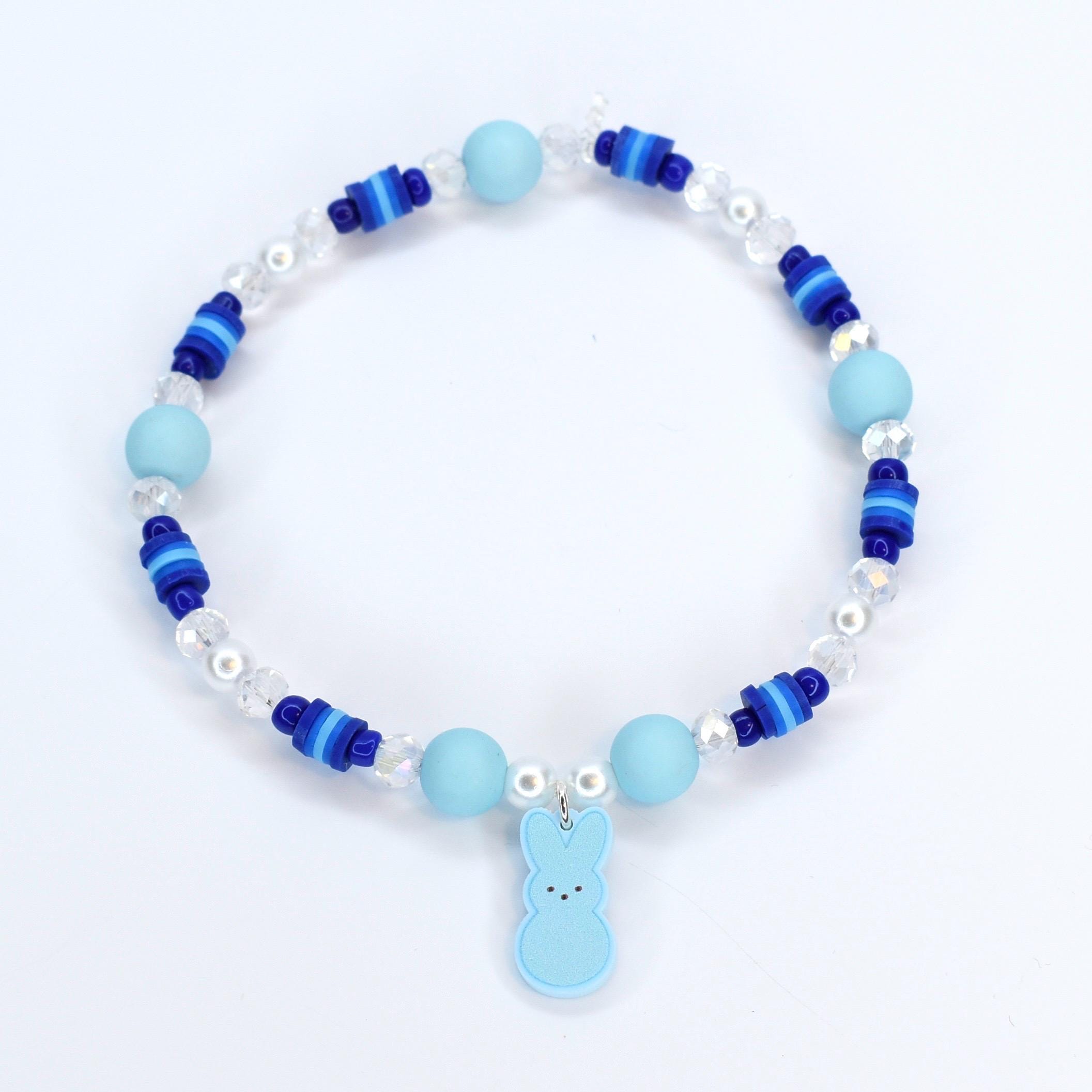 A bracelet with pastel blue and blue gradient heishi beads with crystal and pearl accent beads. A pastel blue PEEPS charm is the focal point of the bracelet.