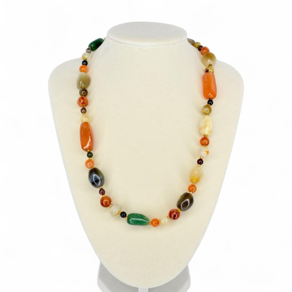 A colorful necklace with a variety of polished stone beads in shades of orange, green, brown, and yellow. The necklace is displayed on a white mannequin bust, showcasing its design and color variations.