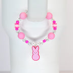 A pink beaded tumbler handle bracelet with a Peep-shaped charm. The bracelet features large pink beads, clear crystal beads, and small pink and white accent beads. The charm is a pink bunny with a pink outline.