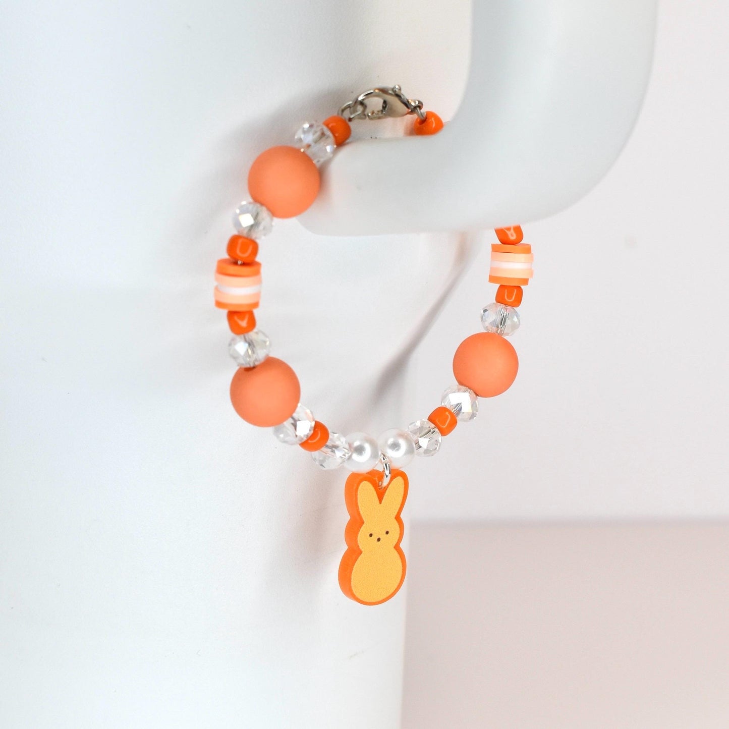 Orange beaded bracelet with a charm shaped like a yellow and orange marshmallow chick. The bracelet features orange, clear, and white beads. The bracelet is secured with a silver clasp.