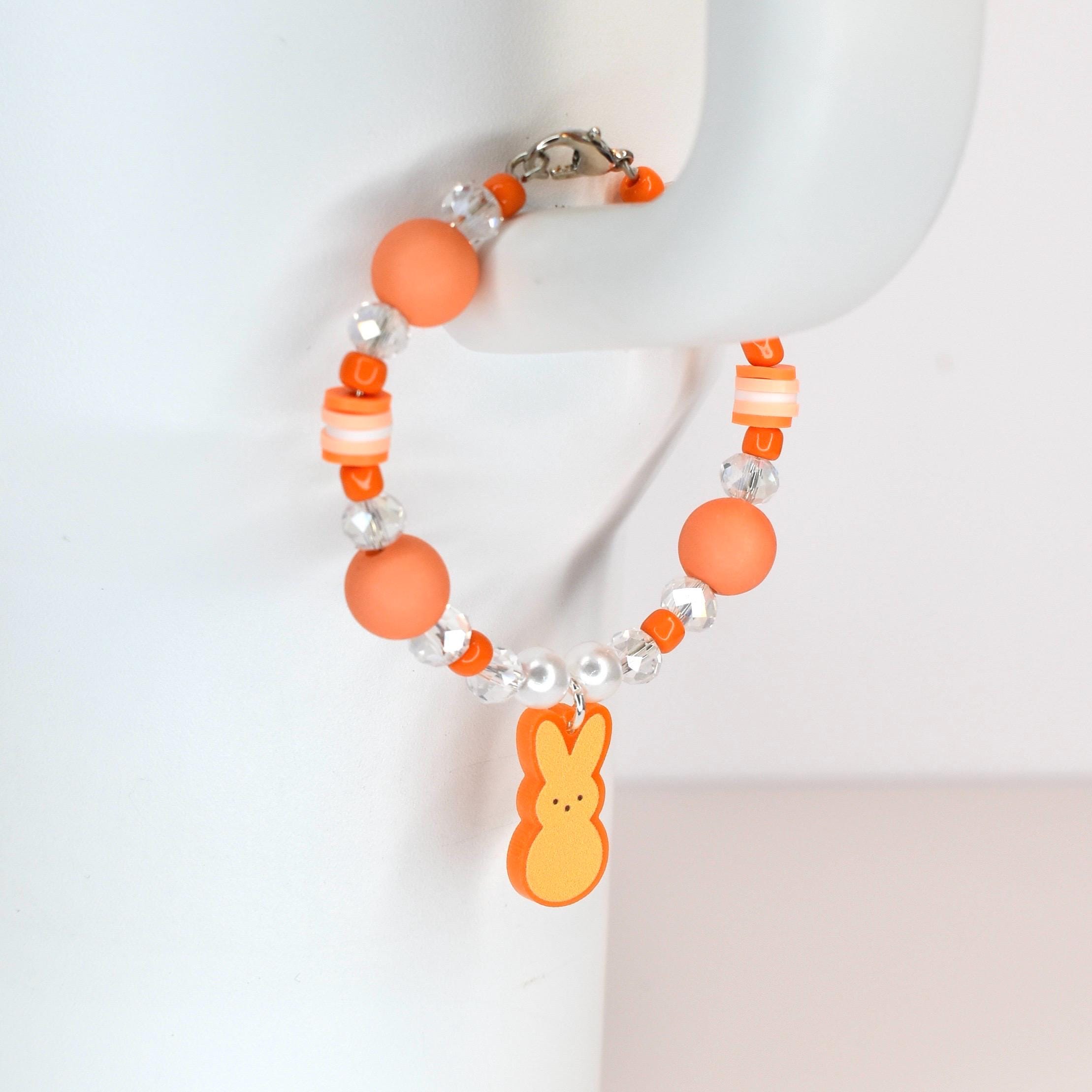 Orange beaded bracelet with a charm shaped like a yellow and orange marshmallow chick. The bracelet features orange, clear, and white beads. The bracelet is secured with a silver clasp.