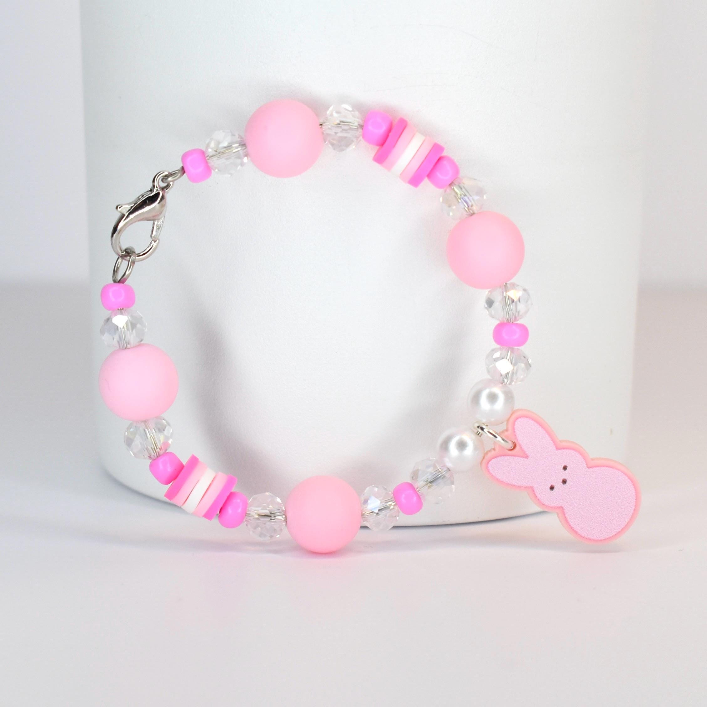 A pink beaded bracelet with a silver clasp. The bracelet features large pink beads, clear crystal beads, and small pink and white accent beads. A pink bunny charm hangs from the bracelet.