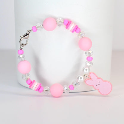 A pink beaded bracelet with a silver clasp. The bracelet features large pink beads, clear crystal beads, and small pink and white accent beads. A pink bunny charm hangs from the bracelet.