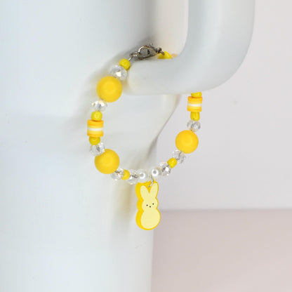 A yellow beaded bracelet with a Peep charm. The bracelet features yellow and clear beads, with a lobster clasp closure. The charm is a yellow Peep bunny with three small dots for eyes.