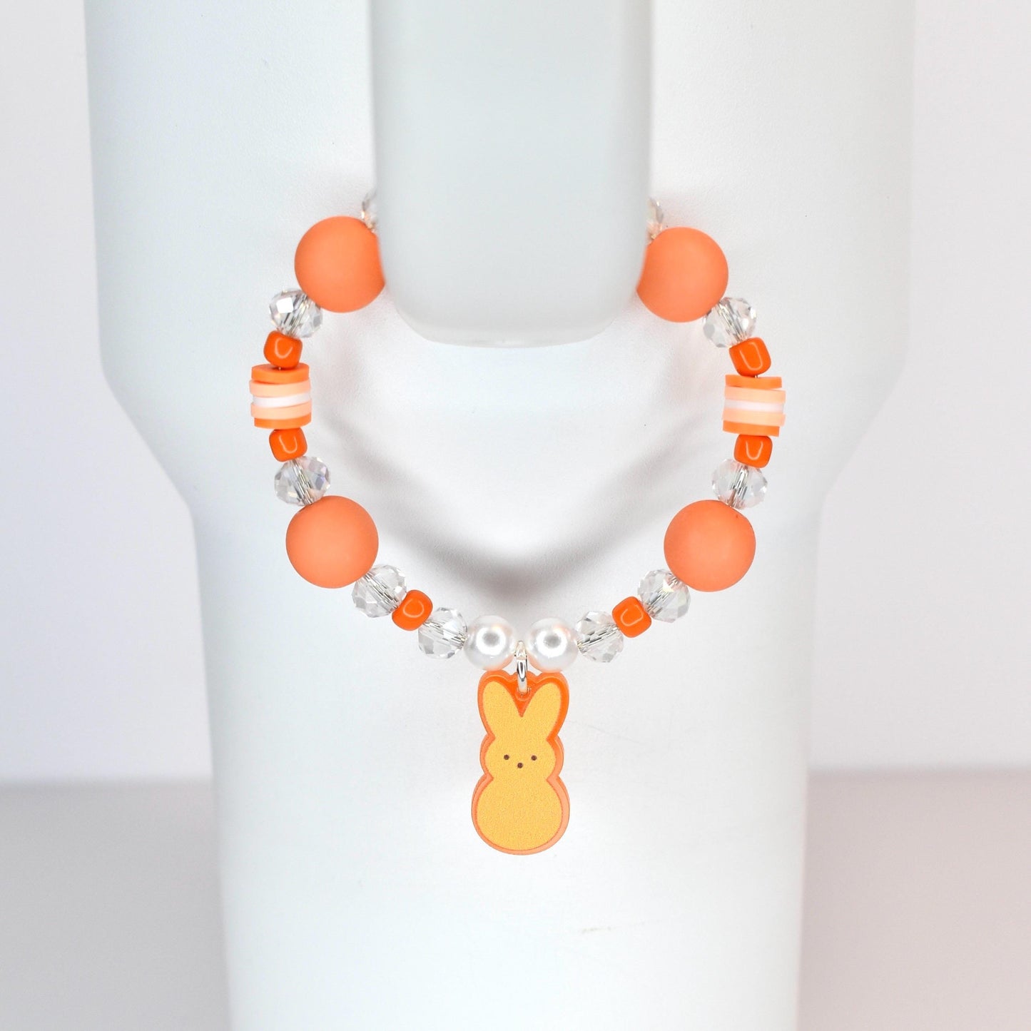 Orange beaded bracelet with a Peep charm. The bracelet features large orange beads, clear crystal beads, and small white beads. The charm is a yellow and orange Peep bunny. The bracelet is displayed on a white surface.