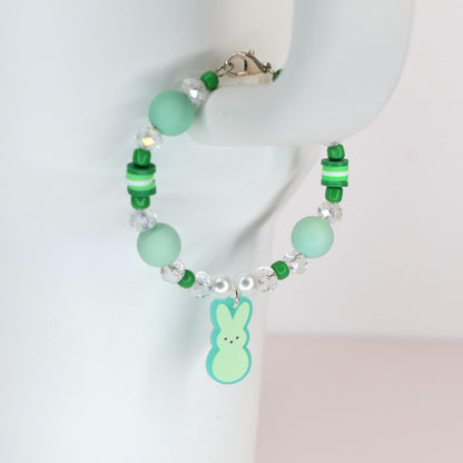 A beaded bracelet with a light green Peep charm. The bracelet features light green and clear beads, with a silver clasp. The bracelet is a spring-themed accessory.