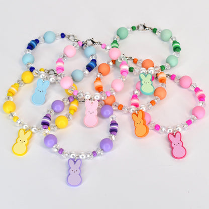 A collection of colorful beaded bracelets with various pastel-colored beads and clear crystal accents. Each bracelet features a charm shaped like a bunny in shades of yellow, blue, pink, orange, green, and purple.