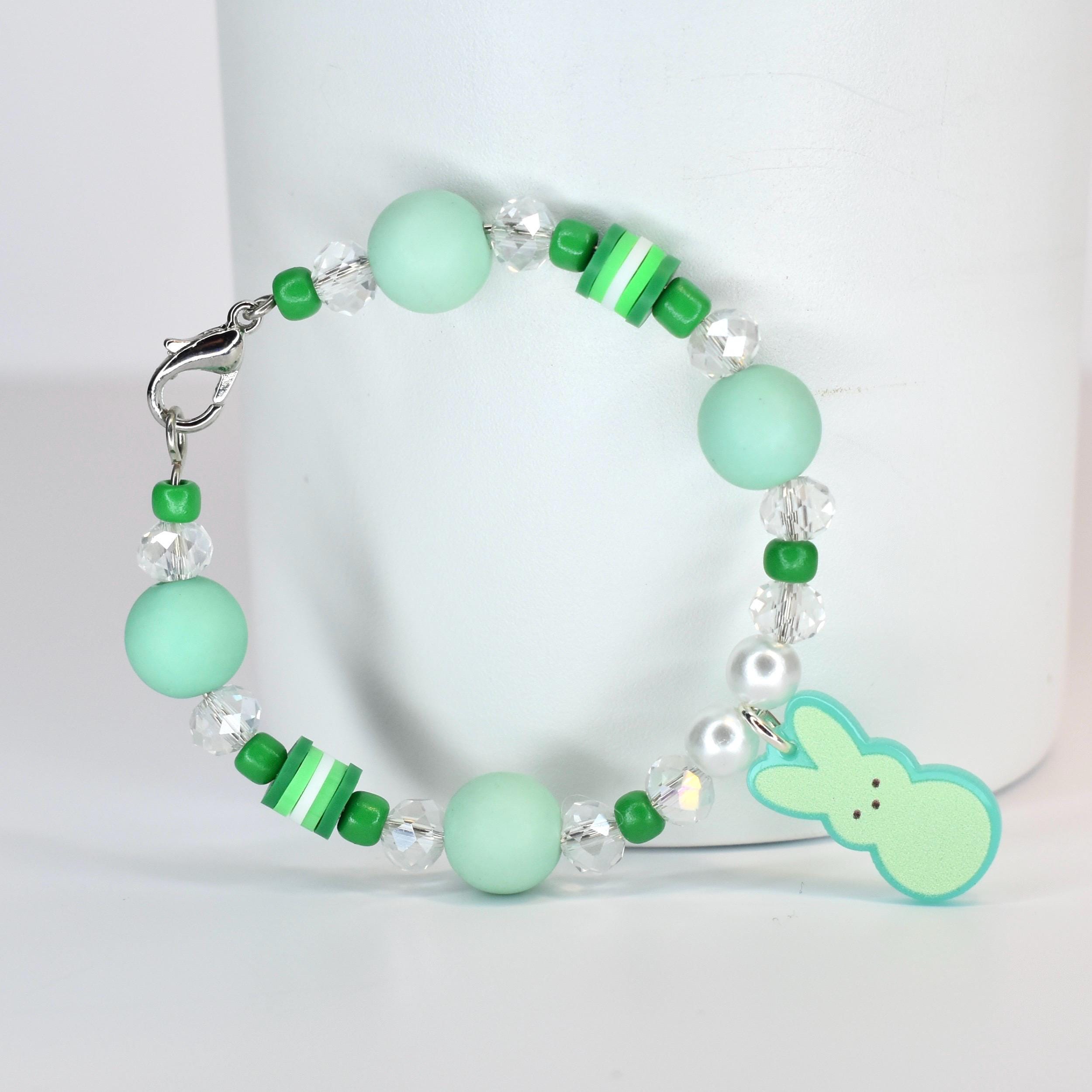 A beaded bracelet featuring mint green and clear beads, with a small bunny charm. The bracelet includes round and cylindrical beads in shades of green and white, and is secured with a silver clasp.