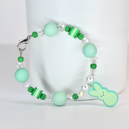 A beaded bracelet featuring mint green and clear beads, with a small bunny charm. The bracelet includes round and cylindrical beads in shades of green and white, and is secured with a silver clasp.