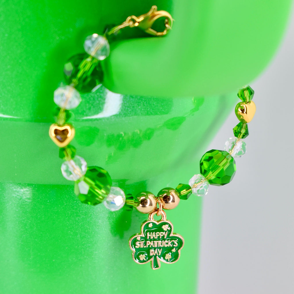 A green beaded bracelet with gold accents and a charm that says "Happy St. Patrick's Day." The bracelet features clear and green beads, with a gold heart-shaped charm. The bracelet is attached to a gold clasp.