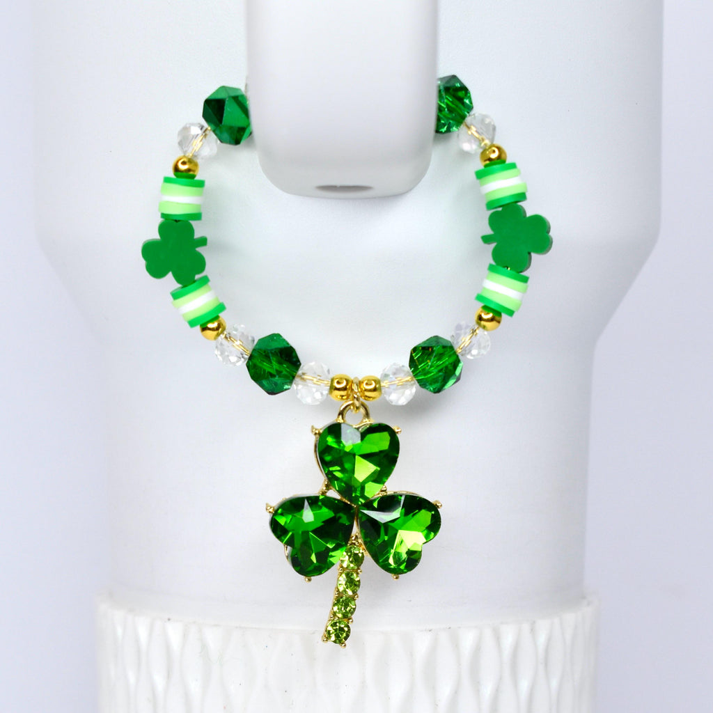 A St. Patrick's Day themed tumbler handle bracelet with a green shamrock pendant. The bracelet features green and clear beads, gold accents, and green clover-shaped charms. The pendant is a large, faceted shamrock.