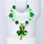 A St. Patrick's Day themed tumbler handle bracelet with a green shamrock pendant. The bracelet features green and clear beads, gold accents, and green clover-shaped charms. The pendant is a large, faceted shamrock.