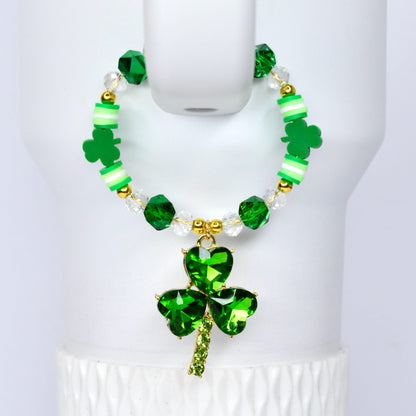A St. Patrick's Day themed tumbler handle bracelet with a green shamrock pendant. The bracelet features green and clear beads, gold accents, and green clover-shaped charms. The pendant is a large, faceted shamrock.