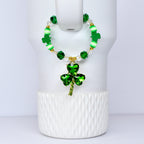 A green beaded bracelet with a shamrock pendant. The bracelet features green, white, and clear beads, with gold accents. The shamrock pendant is a vibrant green, with a gold stem. The bracelet is displayed on a white surface.