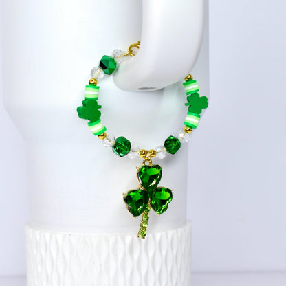 A St. Patrick's Day tumbler bracelet featuring green shamrock charms and beads. The bracelet has a gold-colored clasp and a large, sparkling green shamrock pendant. The beads are green, white, and clear, creating a festive accessory.