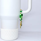 A green and gold beaded bracelet with a charm. The bracelet features various shades of green beads, including round and star-shaped beads, and clear crystal beads. A gold-colored charm hangs from the bracelet.