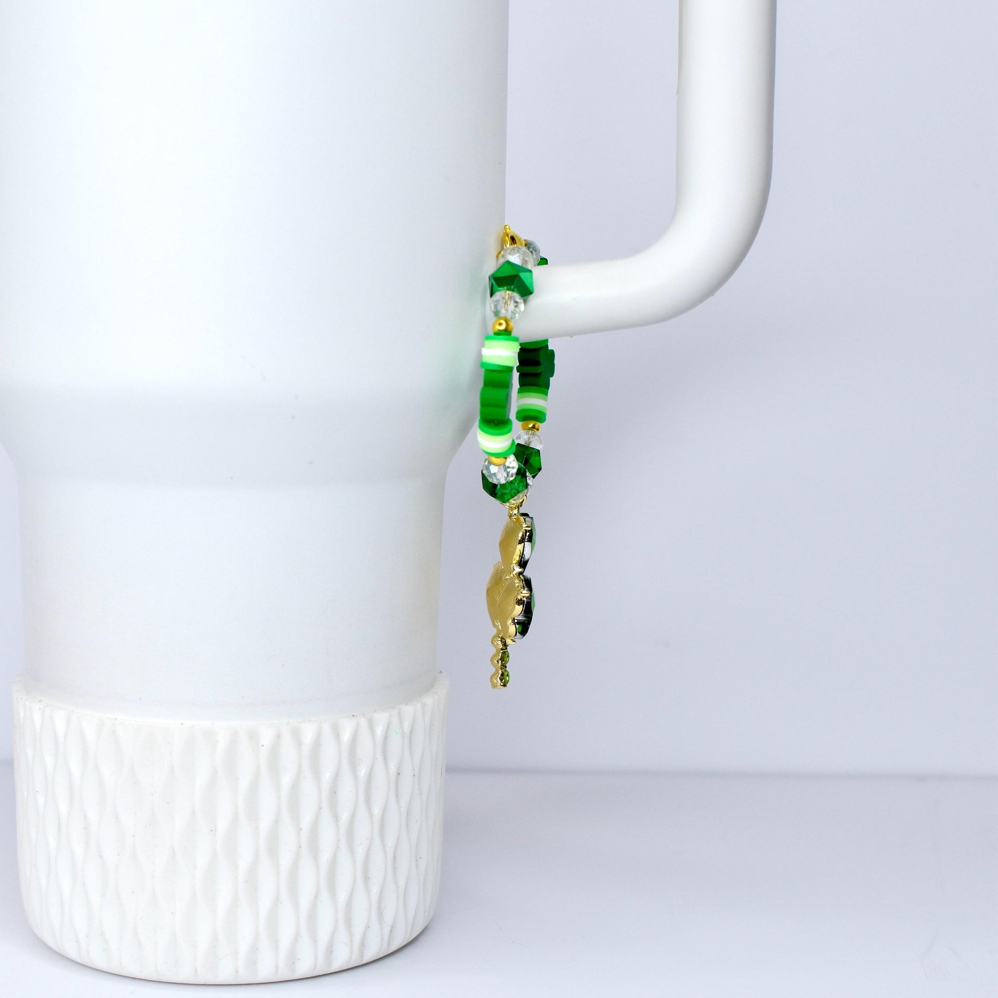 A green and gold beaded bracelet with a charm. The bracelet features various shades of green beads, including round and star-shaped beads, and clear crystal beads. A gold-colored charm hangs from the bracelet.