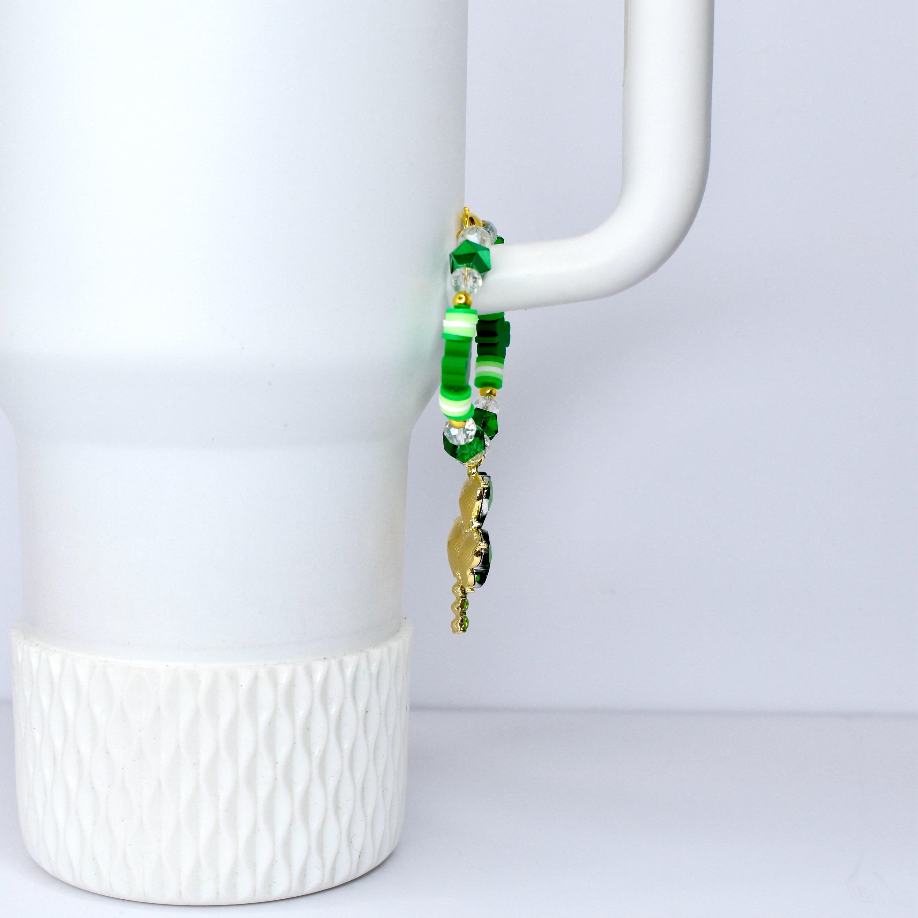 A green and gold beaded bracelet with a charm. The bracelet features various shades of green beads, including round and star-shaped beads, and clear crystal beads. A gold-colored charm hangs from the bracelet.