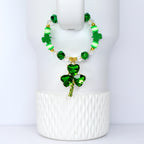 A green beaded bracelet with a shamrock pendant. The bracelet features green, white, and gold beads. The pendant is a three-leaf clover made of green crystals. The bracelet is displayed on a white background.