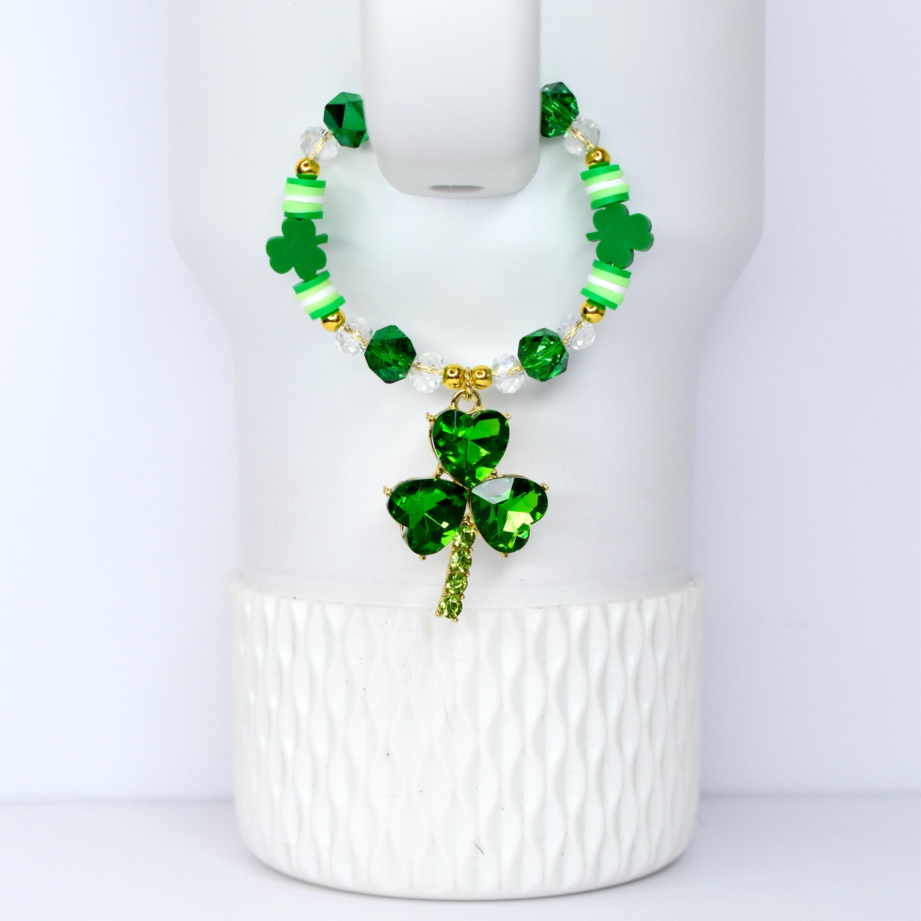 A green beaded bracelet with a shamrock pendant. The bracelet features green, white, and gold beads. The pendant is a three-leaf clover made of green crystals. The bracelet is displayed on a white background.