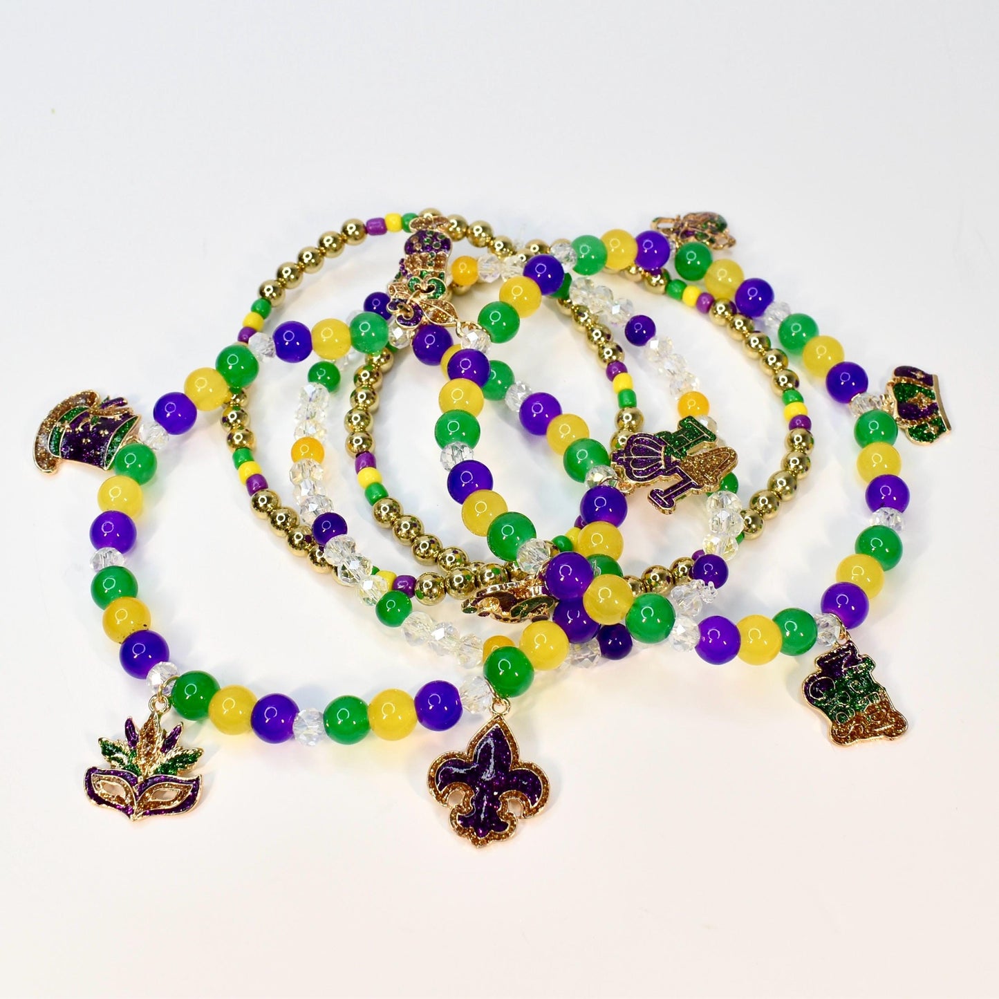 A collection of Mardi Gras beaded necklaces in green, gold, and purple. Each necklace features a variety of beads and decorative charms, including a fleur-de-lis, a mask, and a beer stein.