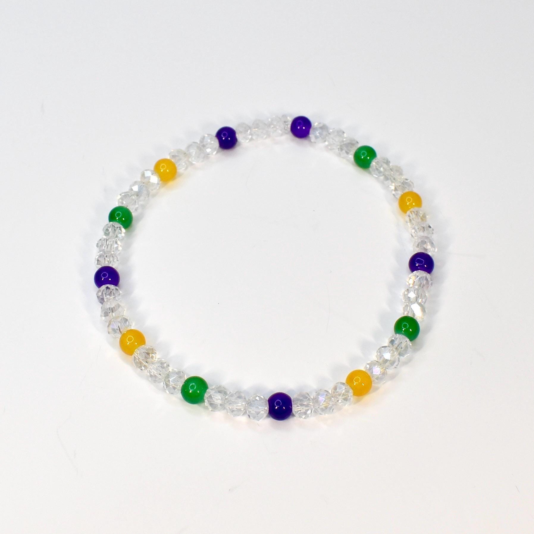 A clear beaded bracelet with alternating colored beads. The bracelet features clear faceted beads interspersed with yellow, green, and purple beads. The bracelet is displayed on a white background.