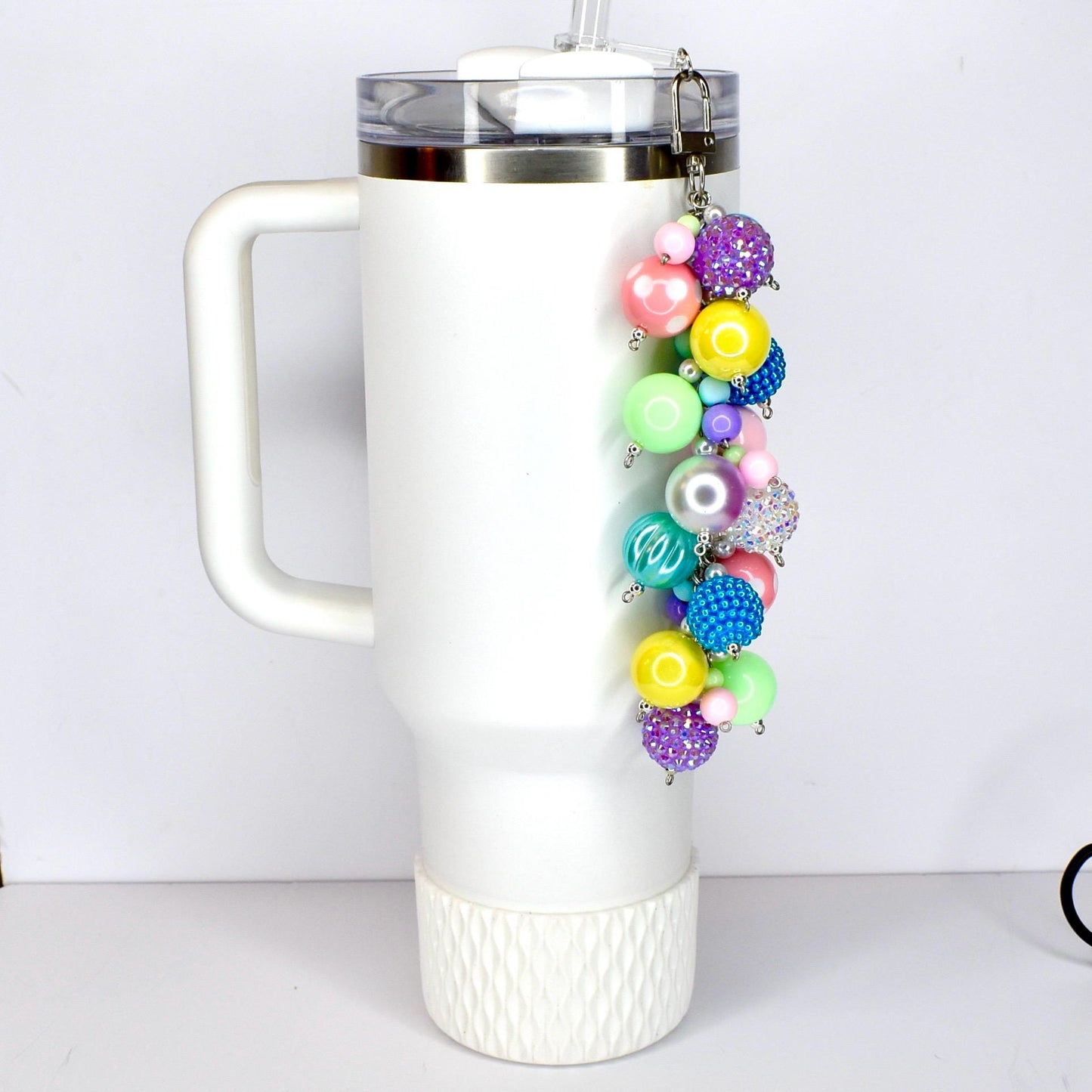 A colorful beaded keychain with a variety of round beads in shades of pink, purple, blue, yellow, and green. The keychain is attached to a white tumbler.