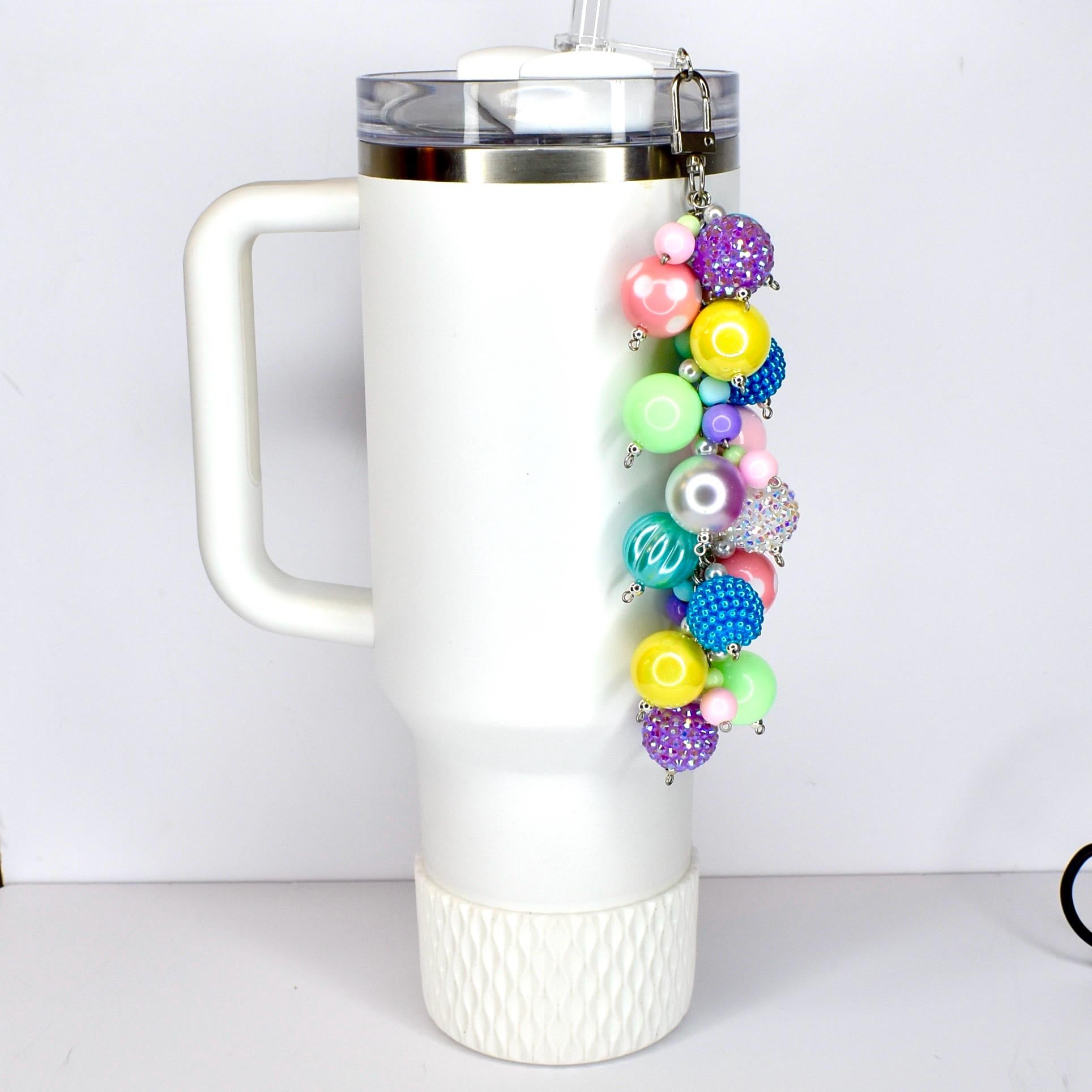 A colorful beaded keychain with a variety of round beads in shades of pink, purple, blue, yellow, and green. The keychain is attached to a white tumbler.
