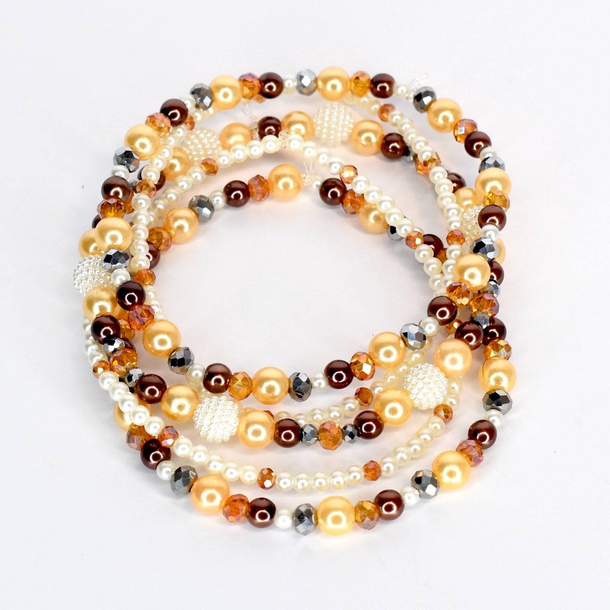 A collection of beaded necklaces in shades of gold, brown, and white. The necklaces feature a variety of bead sizes and textures, including pearls, faceted beads, and round beads. The arrangement is layered and circular.