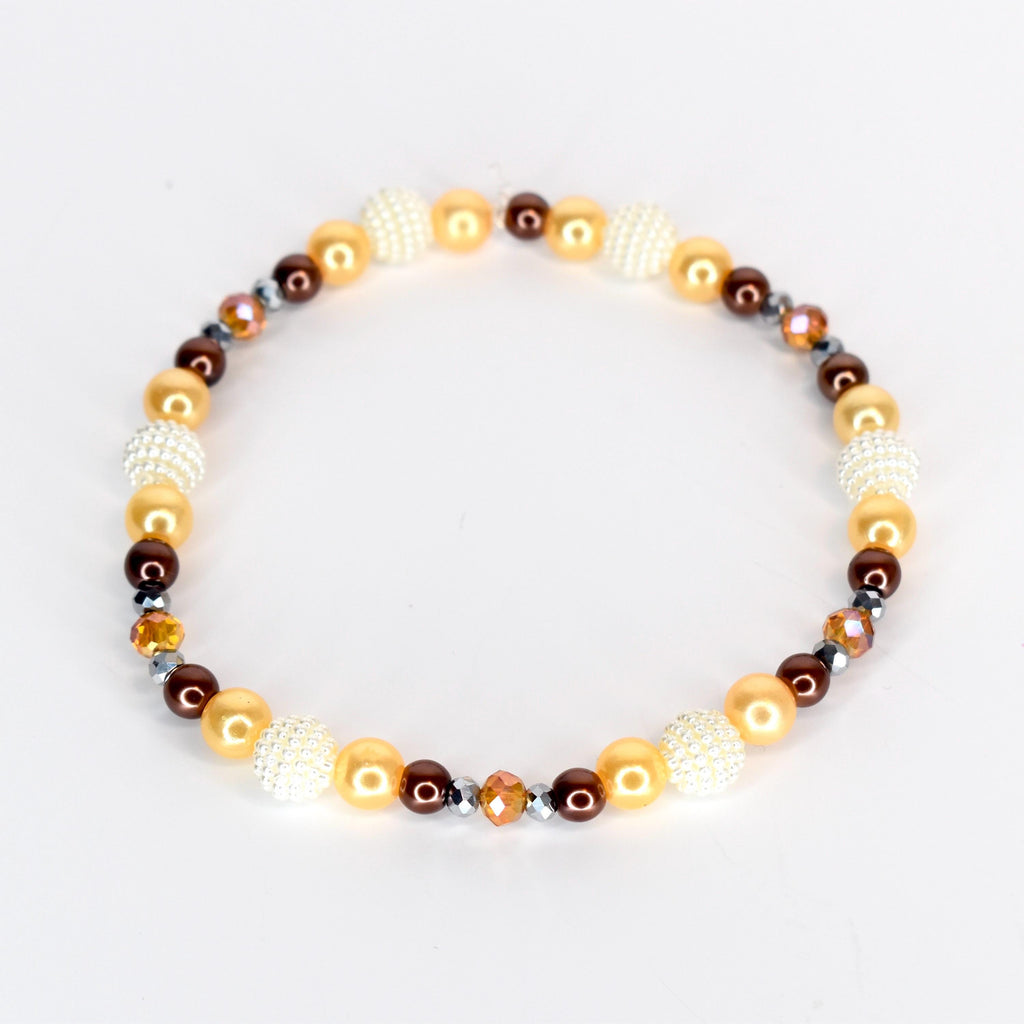 A beaded bracelet featuring a mix of colors and textures. The bracelet includes gold, brown, and white beads, along with faceted crystal accents. The beads are strung together to form a circular shape.