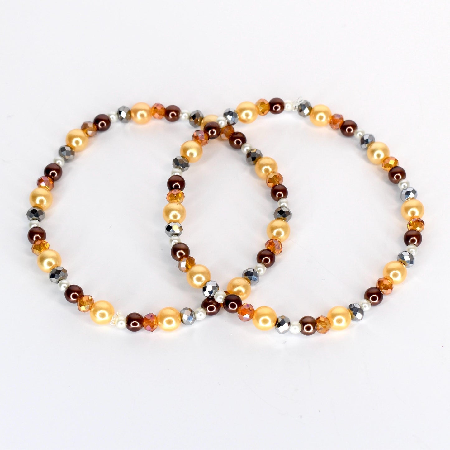 Two beaded bracelets. One bracelet features golden, brown, and silver beads. The other bracelet has a similar design, with golden, brown, and silver beads. The bracelets are on a white background.