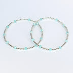 Two delicate bracelets. Each bracelet features small silver beads interspersed with larger, faceted, light blue beads. The bracelets are displayed on a white background, showcasing their simple elegance.