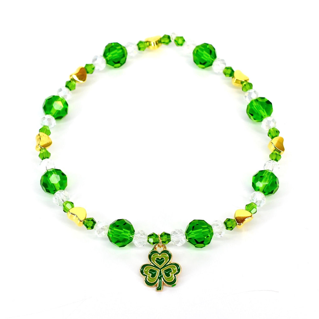 A green and gold beaded bracelet with a shamrock charm. The bracelet features faceted green beads, clear crystal beads, and gold heart-shaped accents. The shamrock charm is green with gold trim.