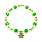 A green and gold beaded bracelet with a shamrock charm. The bracelet features faceted green beads, clear crystal beads, and gold heart-shaped accents. The shamrock charm is green with gold trim.