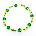 A beaded bracelet featuring alternating green and clear crystal beads, interspersed with small gold heart-shaped charms. The bracelet is strung on a clear elastic cord, creating a delicate and elegant accessory.