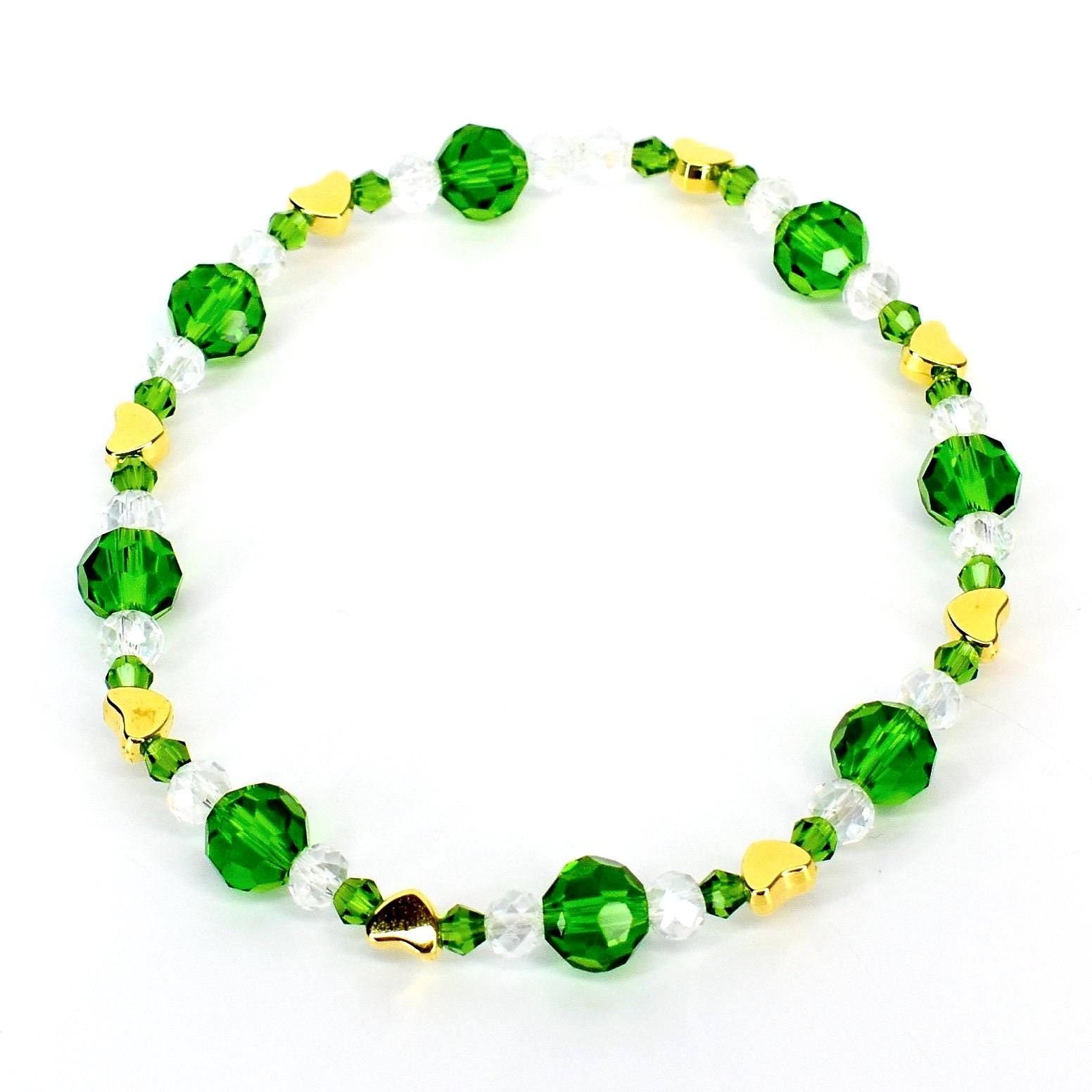A beaded bracelet featuring alternating green and clear crystal beads, interspersed with small gold heart-shaped charms. The bracelet is strung on a clear elastic cord, creating a delicate and elegant accessory.