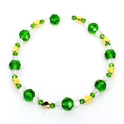 A beaded bracelet featuring alternating green and clear crystal beads, interspersed with small gold heart-shaped charms. The bracelet is strung on a clear elastic cord, creating a delicate and elegant accessory.
