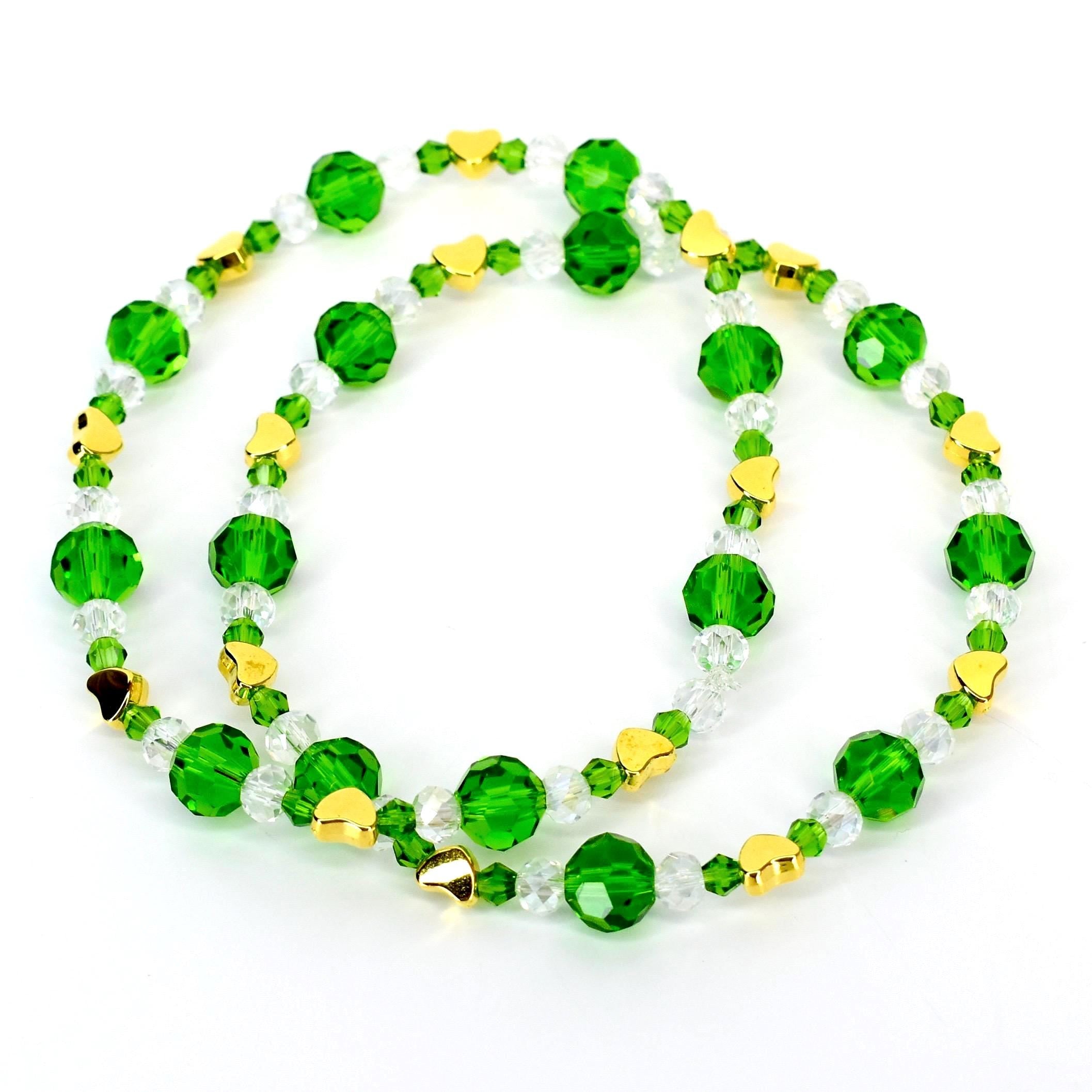 Two beaded necklaces. The necklaces feature faceted green and clear beads, interspersed with small gold-colored heart-shaped charms. The beads are strung on a clear cord. The necklaces are displayed on a white background.