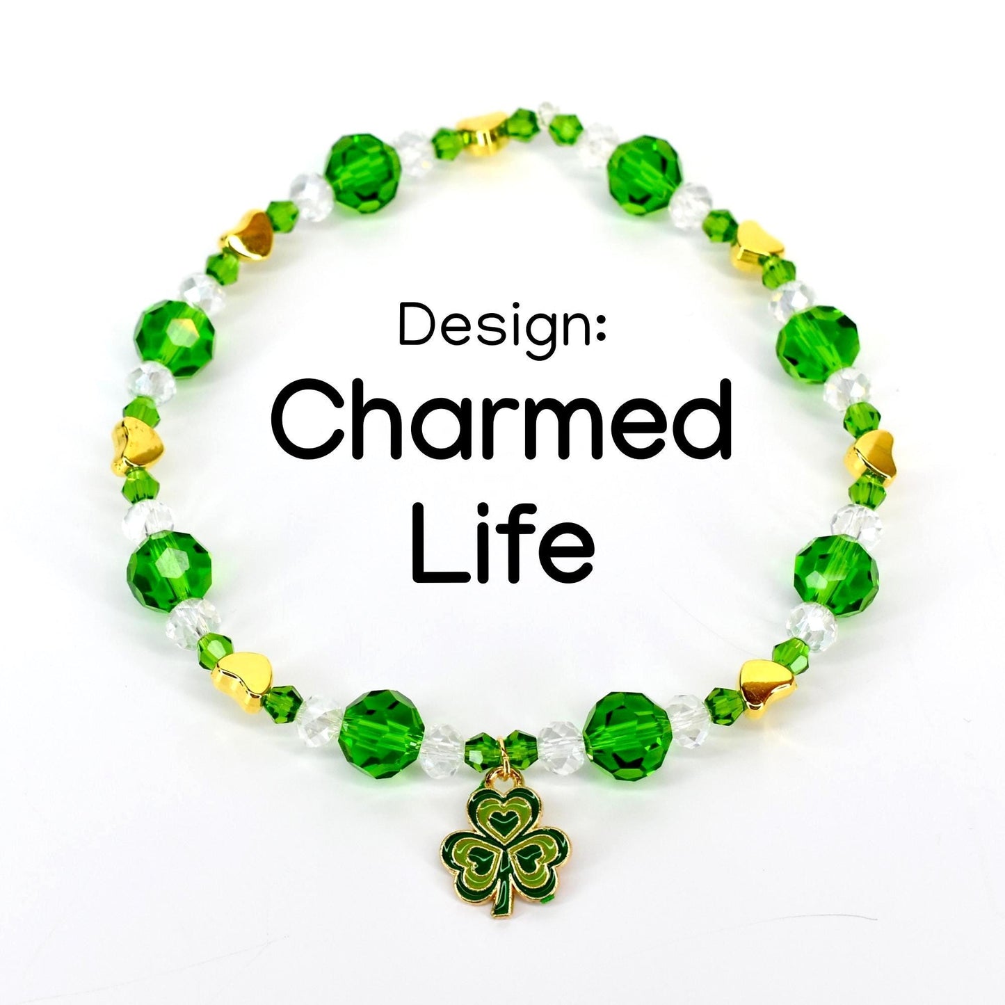 A beaded bracelet with green, clear, and gold beads. The bracelet has a shamrock charm and the text "Design: Charmed Life". The beads are faceted and round, with gold heart-shaped accents.