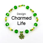 A beaded bracelet with green, clear, and gold beads. The bracelet has a shamrock charm and the text "Design: Charmed Life". The beads are faceted and round, with gold heart-shaped accents.