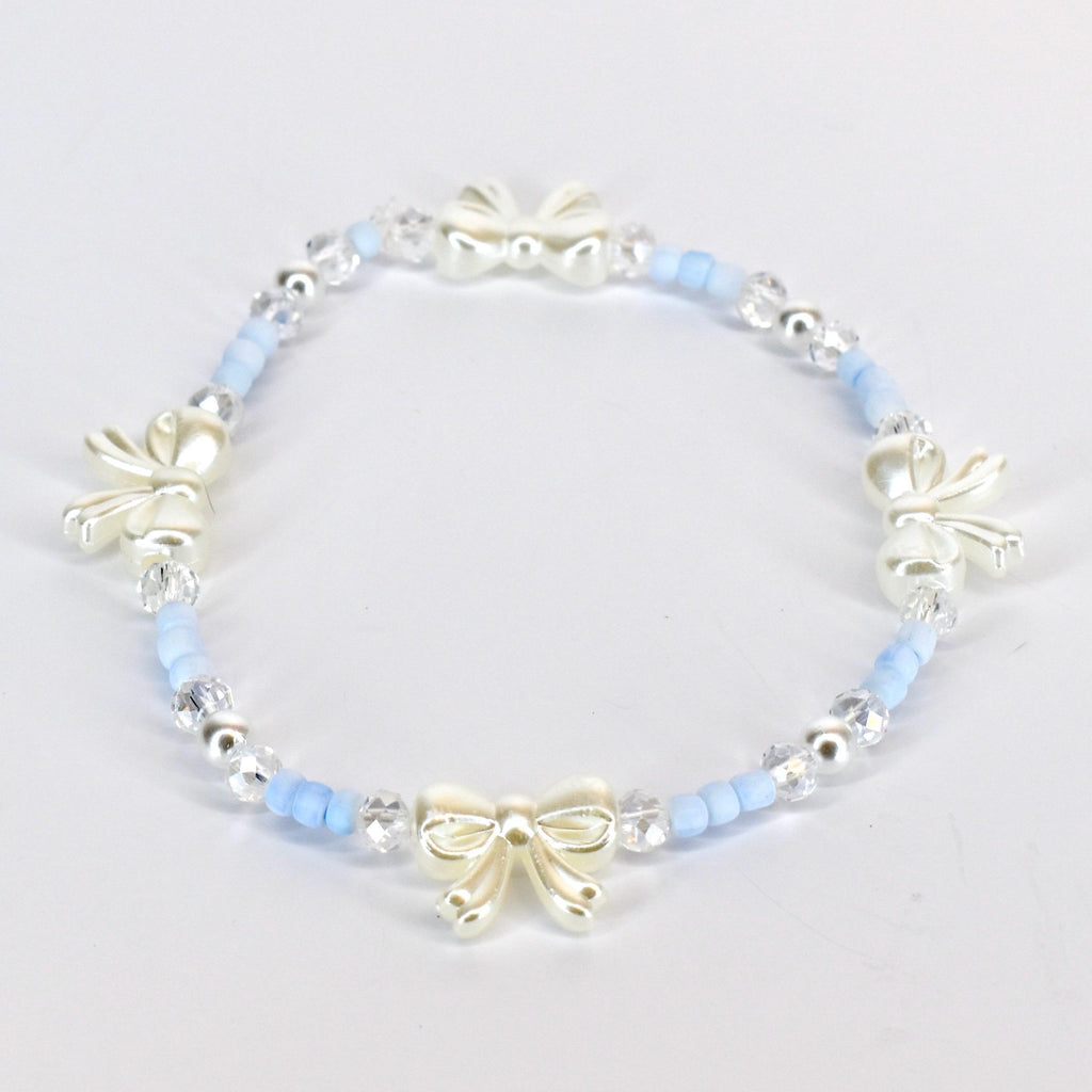 A delicate bracelet featuring a repeating pattern of light blue beads, clear crystal beads, and ivory-colored bow charms. The bracelet is strung on an elastic band, creating a flexible and comfortable fit. The bow charms add a touch of elegance.