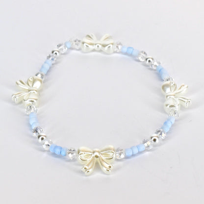 A delicate bracelet featuring a repeating pattern of light blue beads, clear crystal beads, and ivory-colored bow charms. The bracelet is strung on an elastic band, creating a flexible and comfortable fit. The bow charms add a touch of elegance.