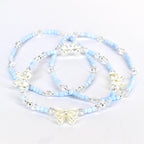 Three delicate bracelets. Each bracelet features light blue beads, clear crystal accents, and a silver-colored bow charm. The bracelets are arranged on a white surface, showcasing their design and details.