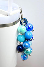 A cluster of blue beaded charms with a silver clasp. The beads vary in size and shade, ranging from light turquoise to deep navy. Some beads have an iridescent sheen, and small silver accents are interspersed throughout.