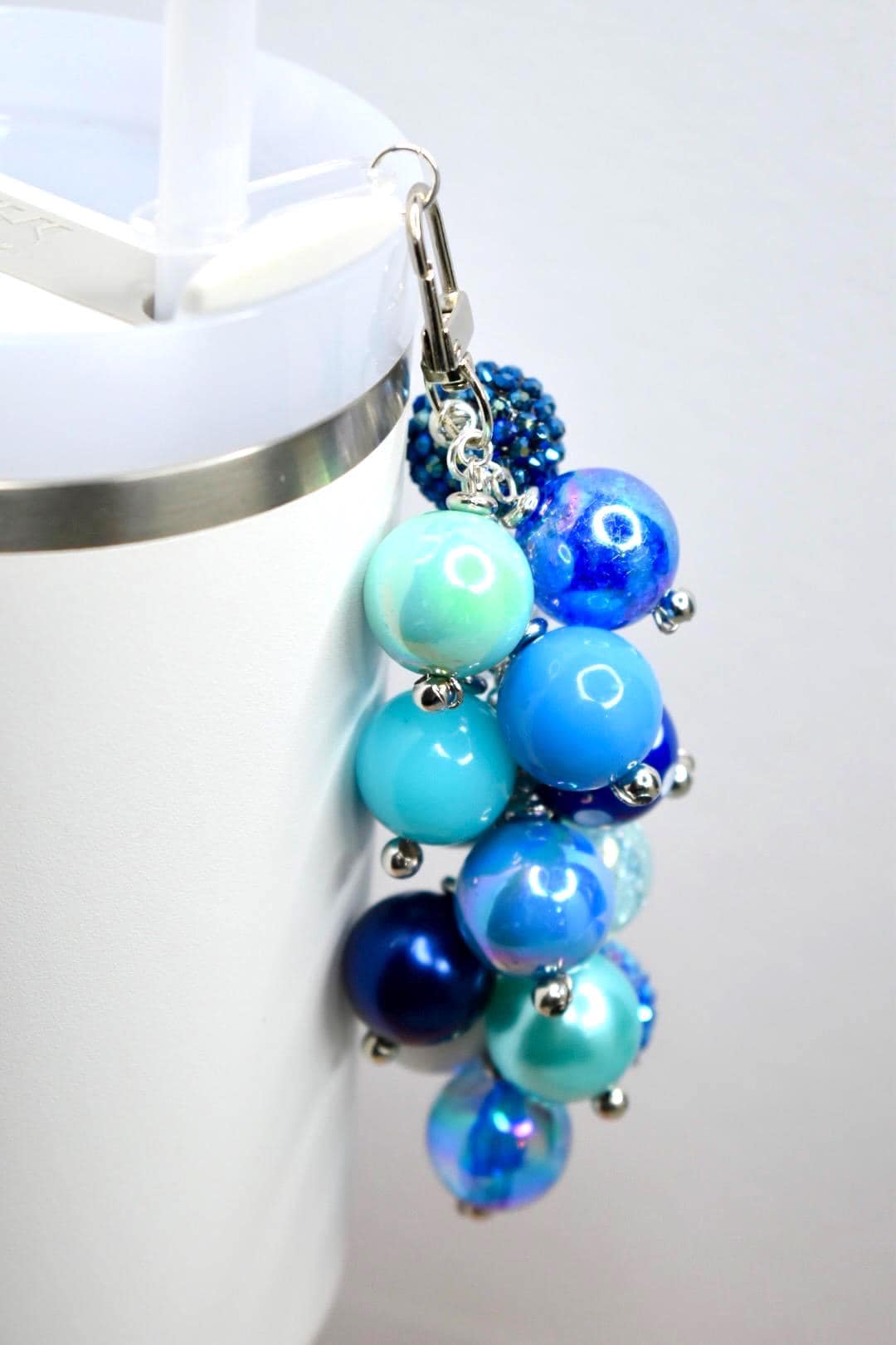 A cluster of blue beaded charms with a silver clasp. The beads vary in size and shade, ranging from light turquoise to deep navy. Some beads have an iridescent sheen, and small silver accents are interspersed throughout.