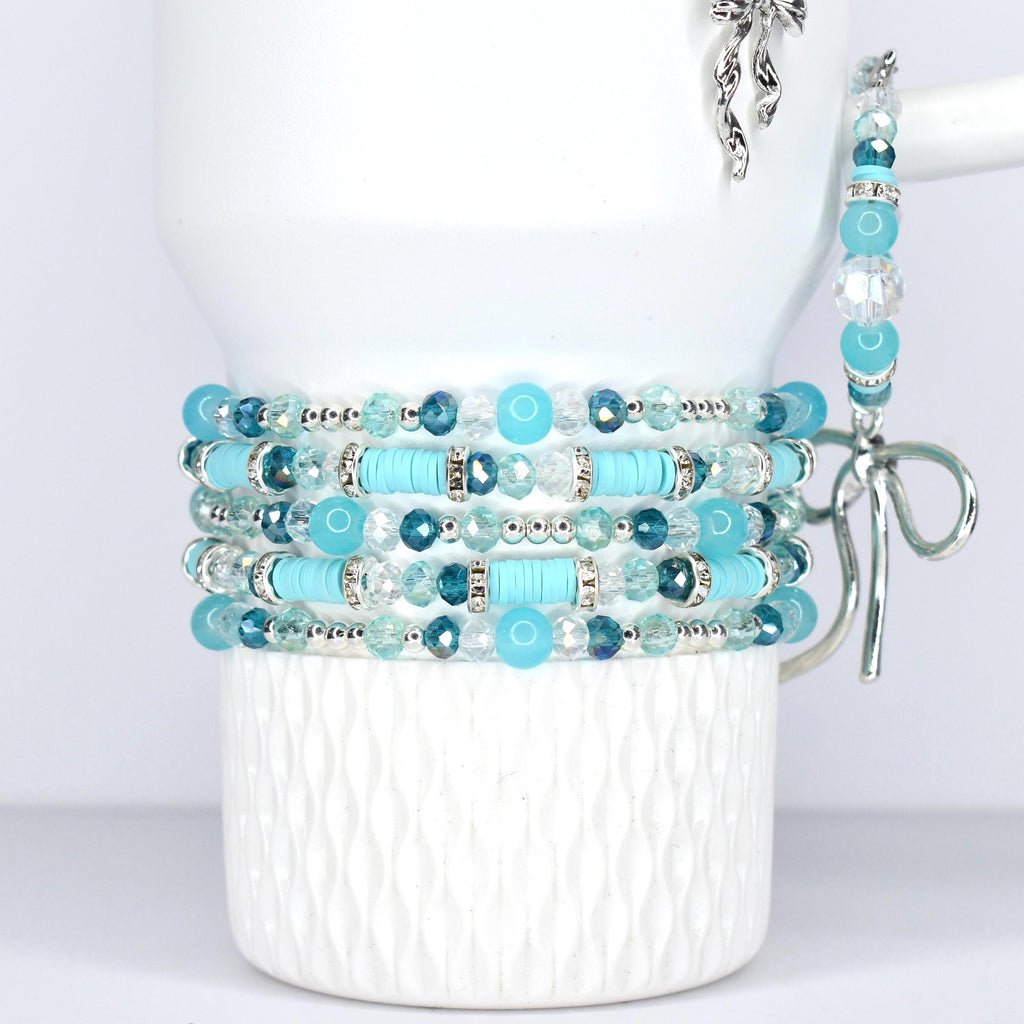 Stack of beaded bracelets in shades of blue and clear. The bracelets feature various bead sizes and shapes, including round, faceted, and disc-shaped beads. The bracelets are displayed on a white tumbler.